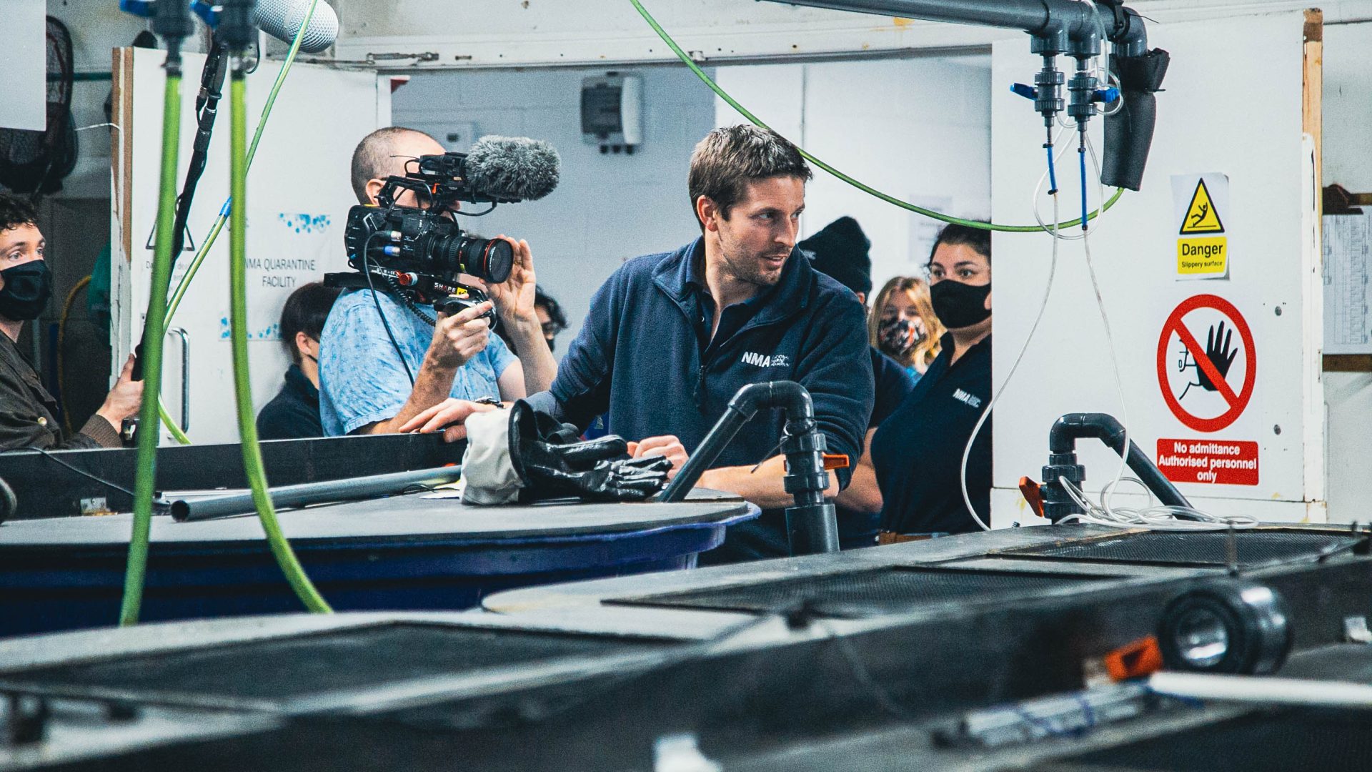 Aquarium curator Marcus standing in front of a tank whilst a film crew follow and film him