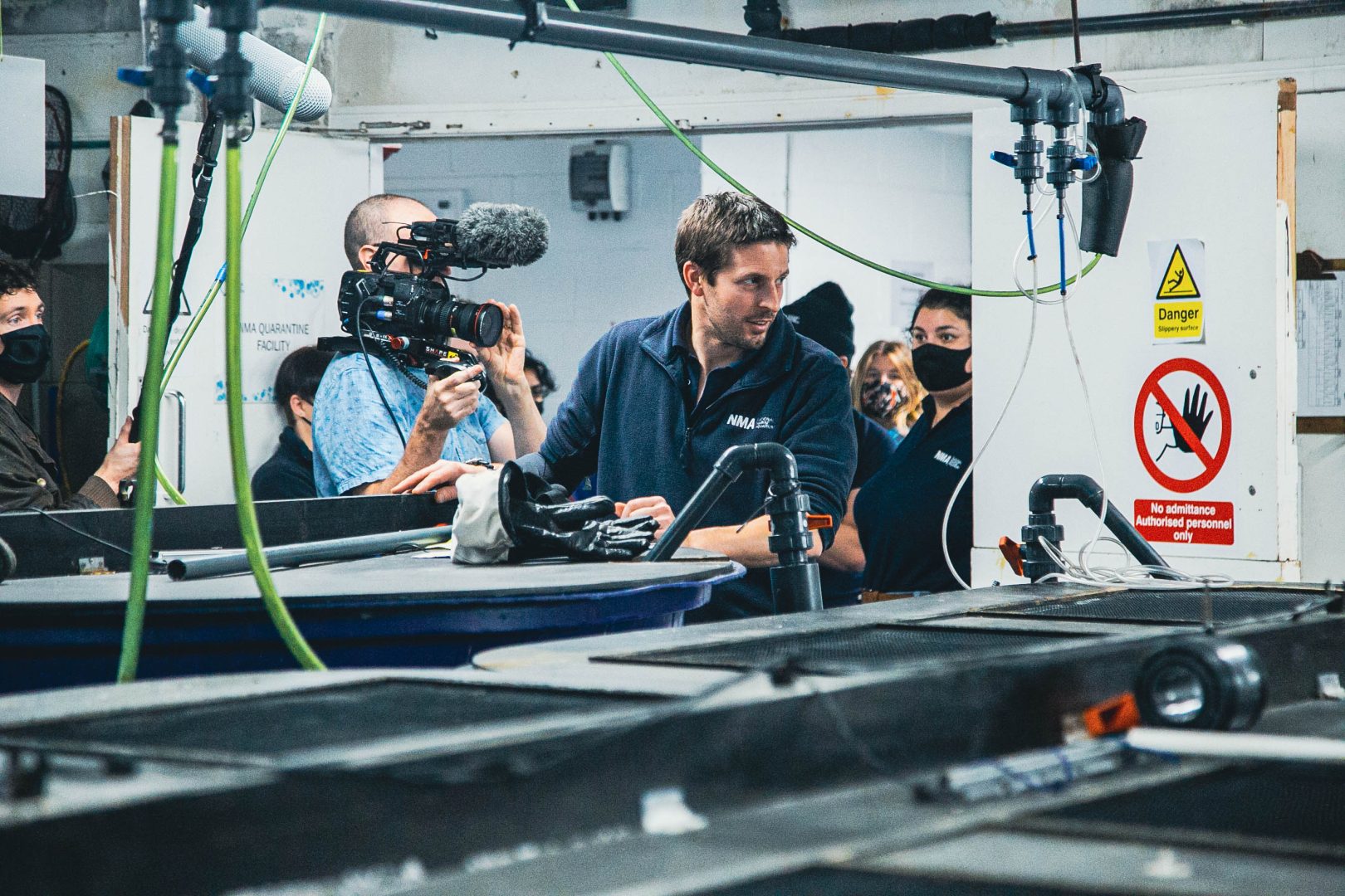 Aquarium curator Marcus standing in front of a tank whilst a film crew follow and film him